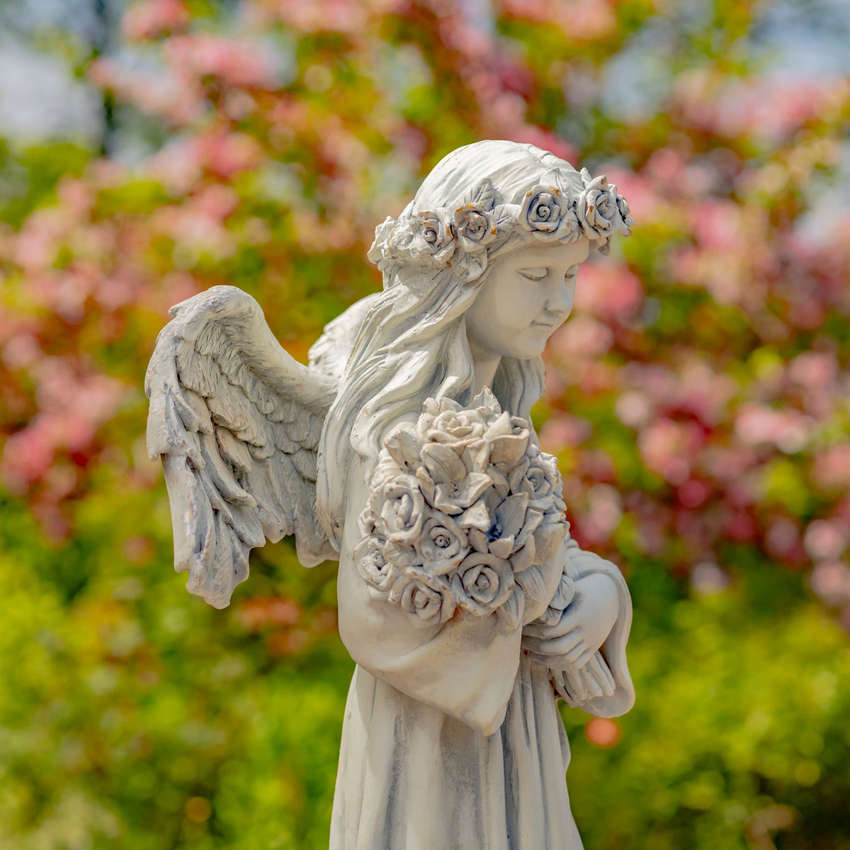 Side view of the angel statue showing its feathered wing, rose crown, and bouquet.