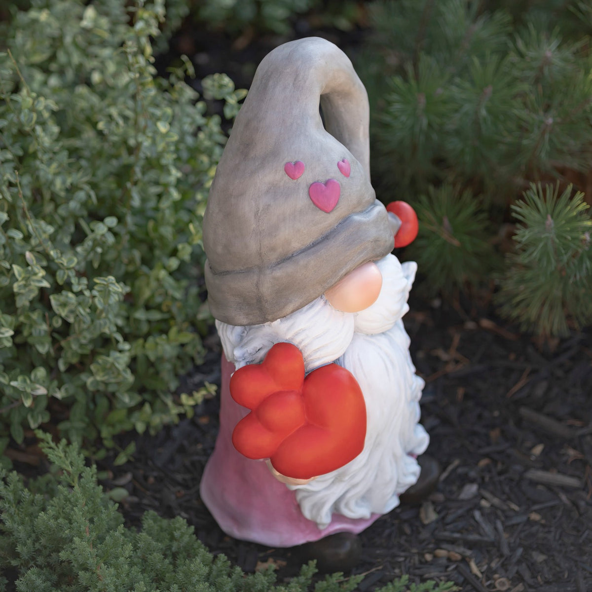 Angled view of the gnome holding a red heart, with a long white beard and gray hat.