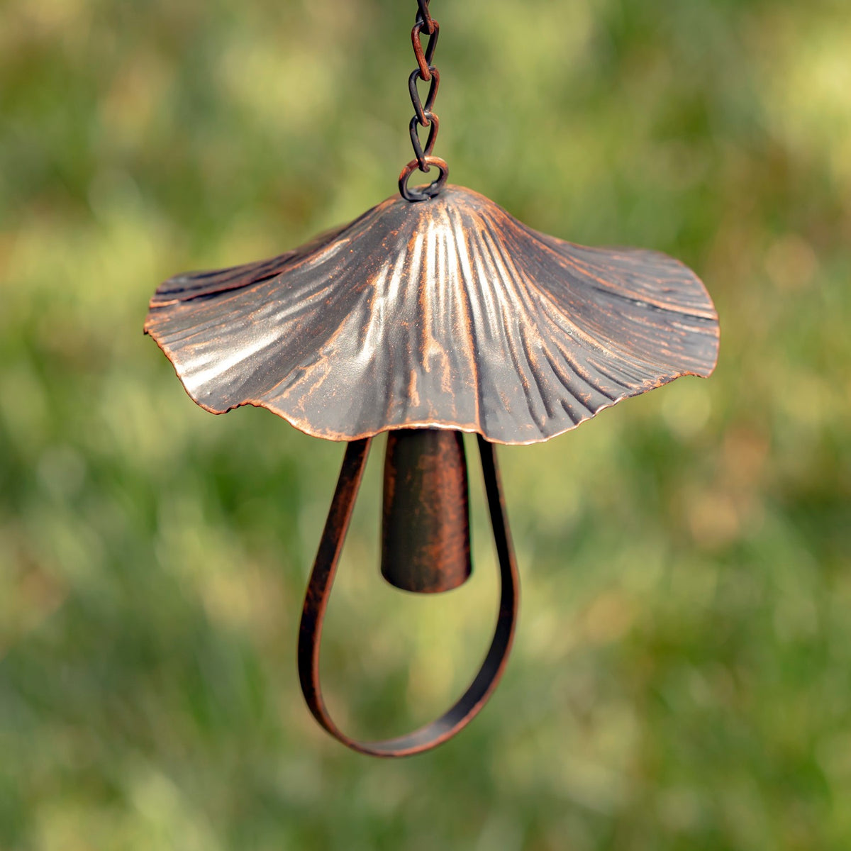 Close-up of an antique bronze mushroom-shaped bell and chain against greenery