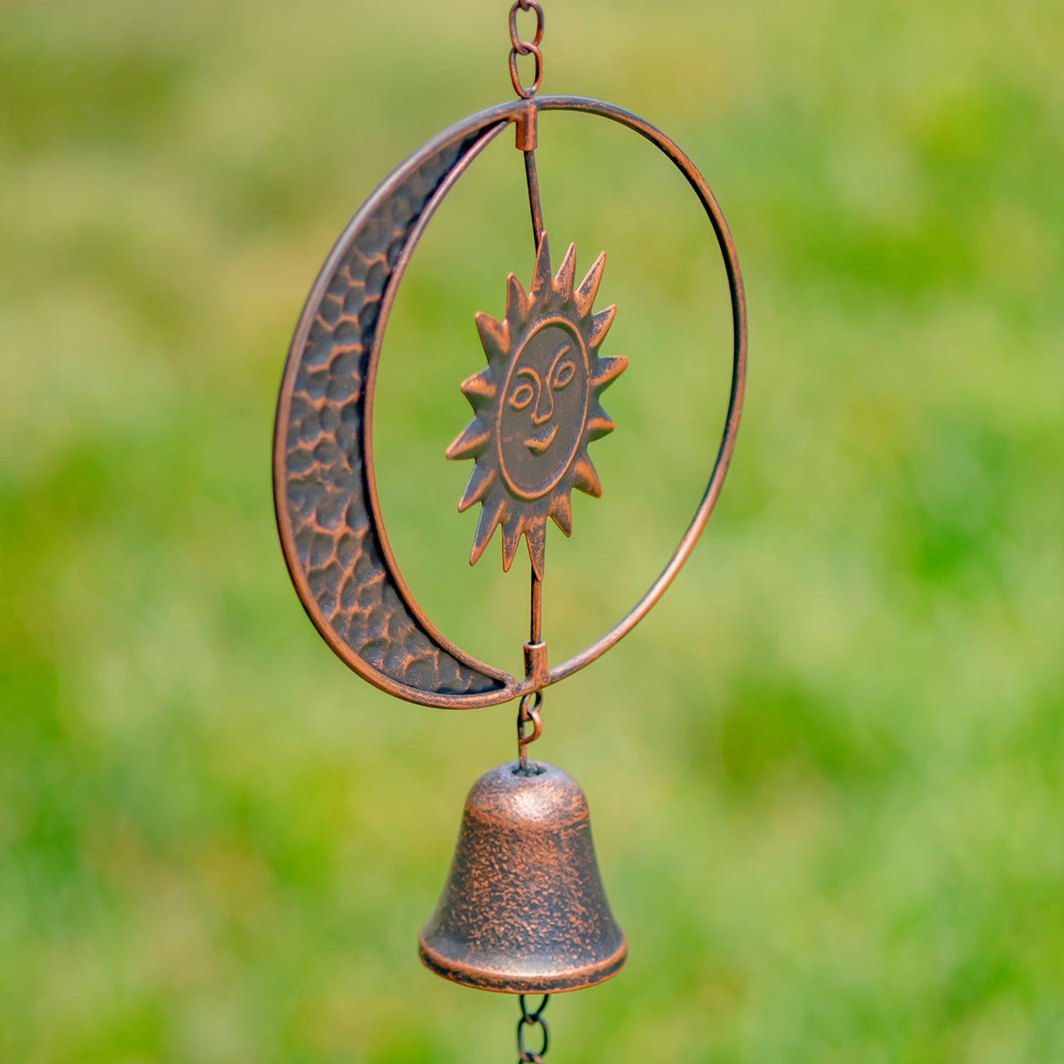 Close view of an antique bronze sun and crescent moon ornament with a hanging bell