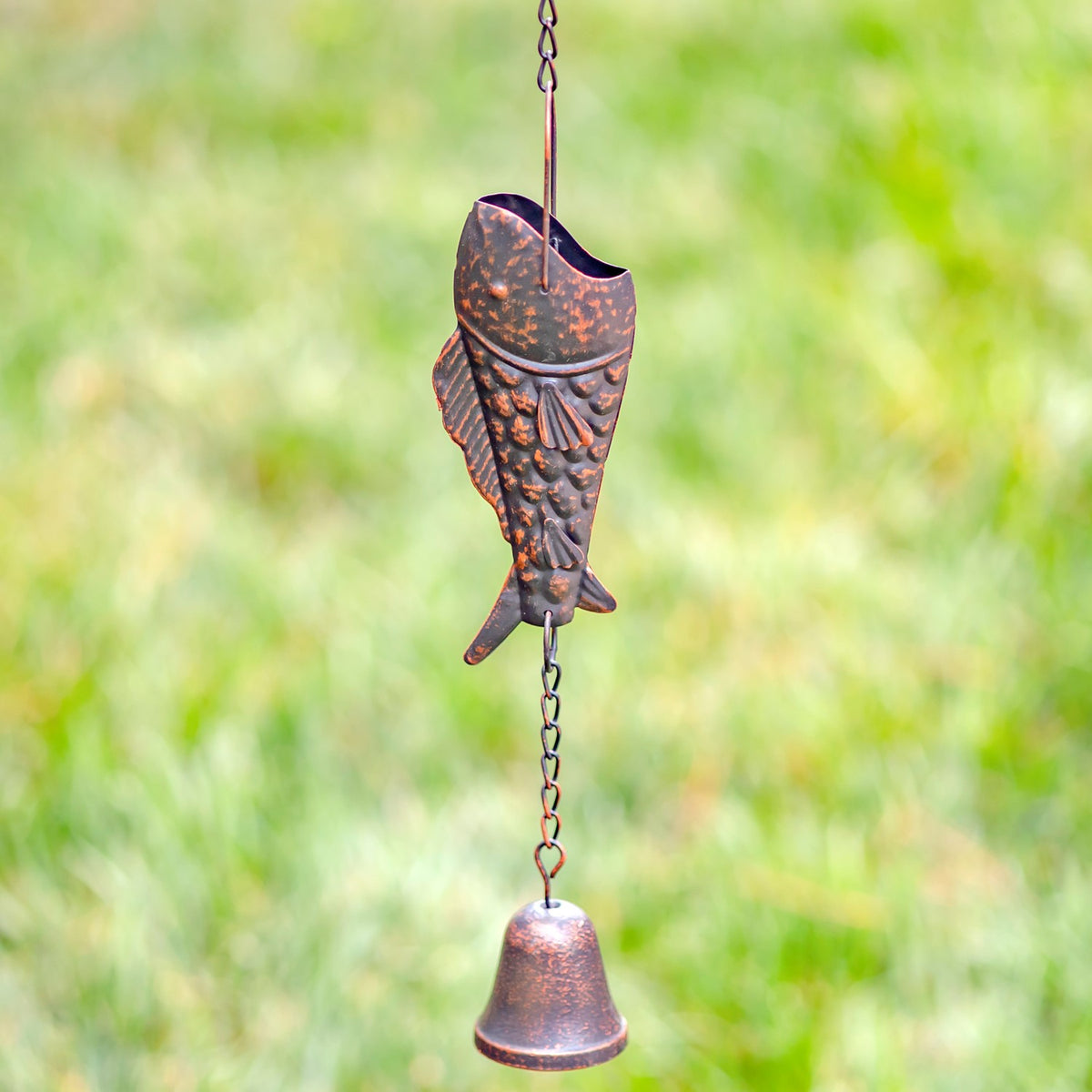 Close view of an antique bronze trout rain chain with a hanging bell