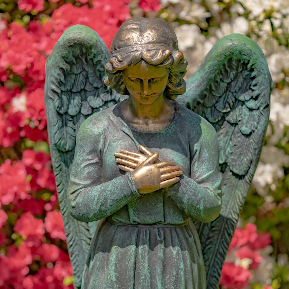 Closer view of the angel's bowed head, feathered wings, and crossed hands against its robe.