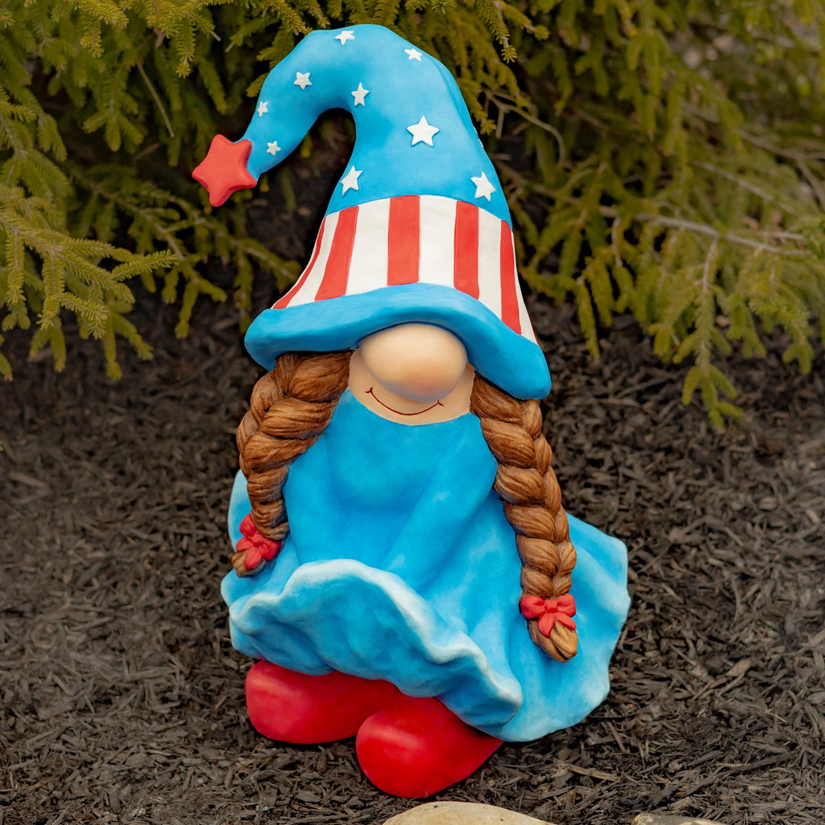 A seated gnome in a starry blue hat and blue dress sits outdoors with long braided hair and red shoes.