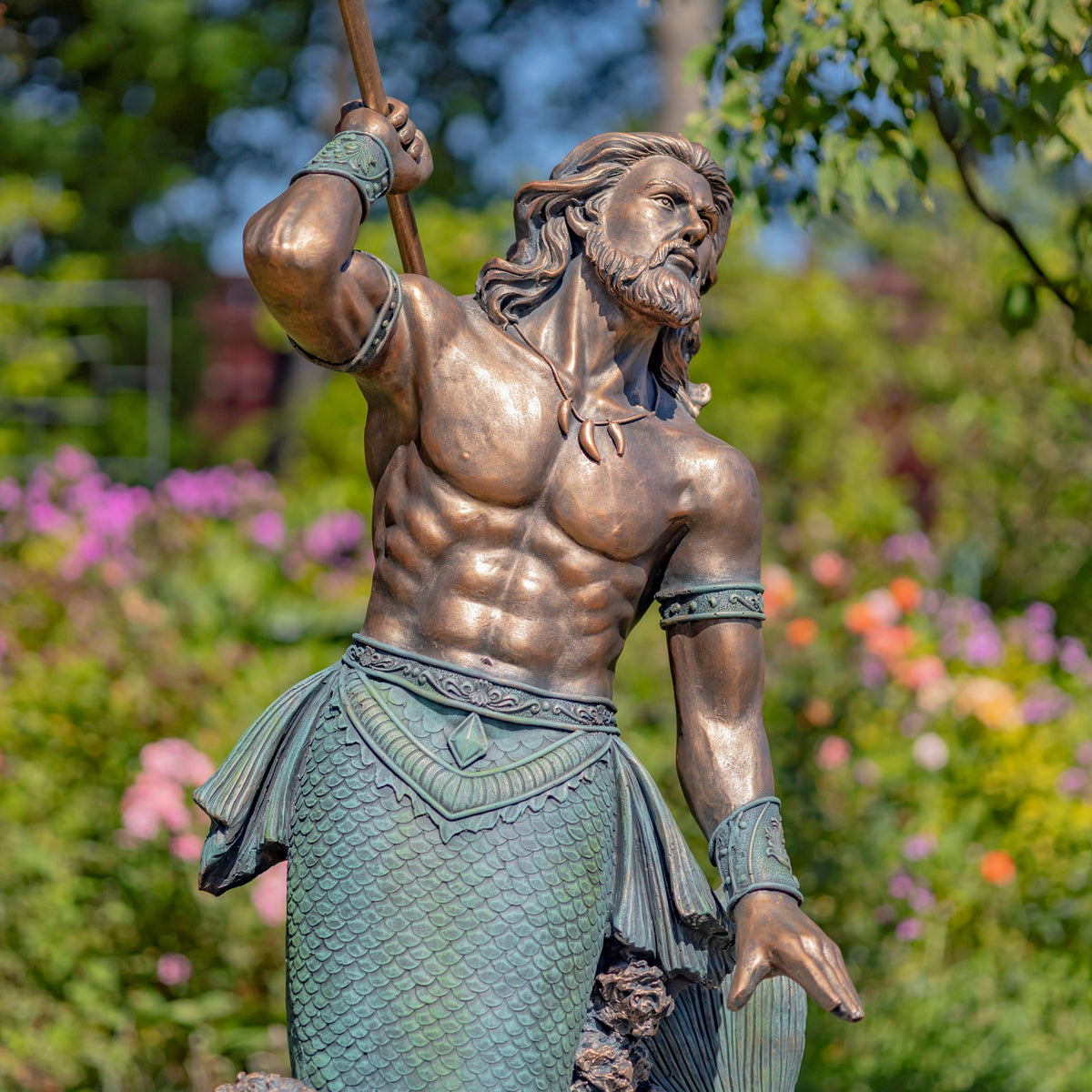 Close view of the merman’s bearded face, muscular torso, arm bands and patterned fish tail.