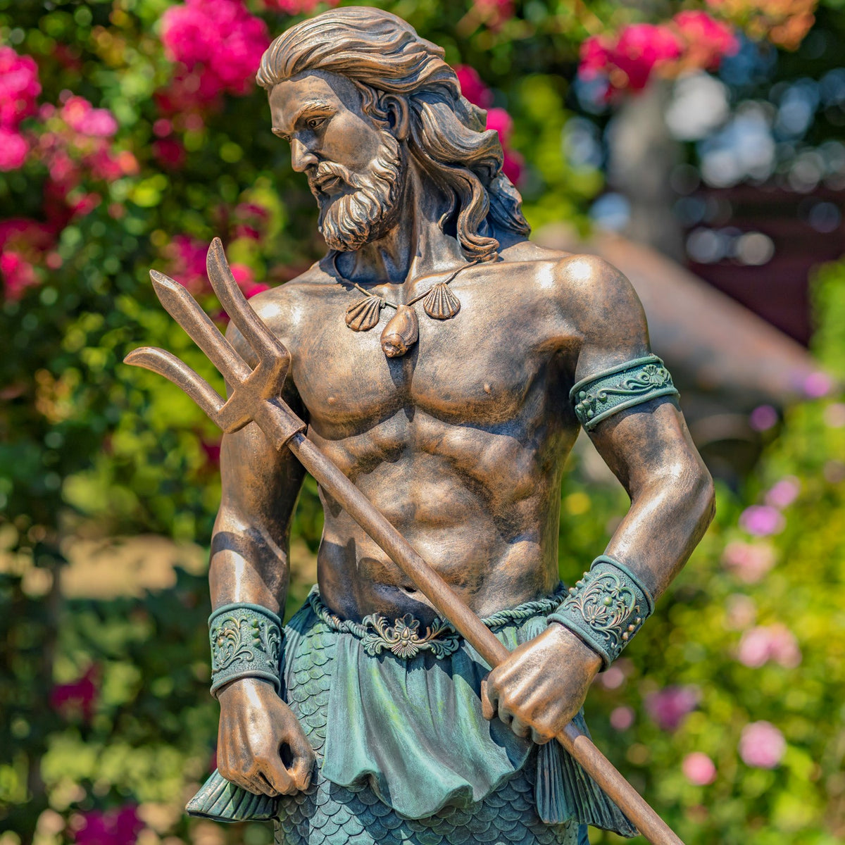 Close view of the merman’s bearded face, muscular torso, ornate cuffs, and trident against garden flowers.