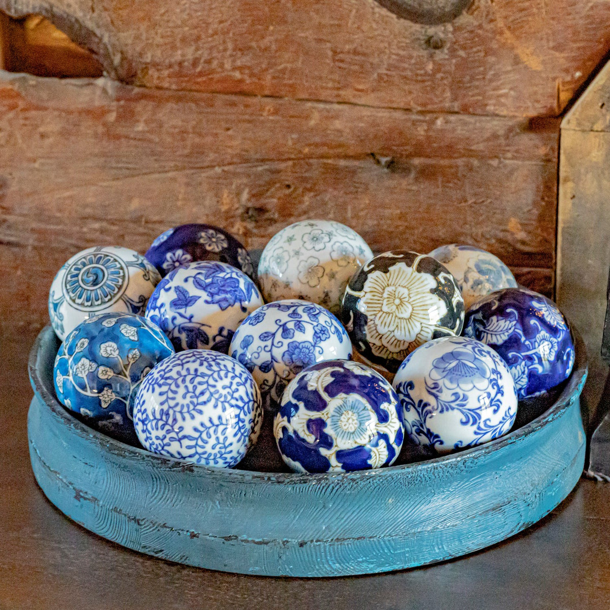 A close view of assorted floral and patterned ceramic balls filling a blue bowl.