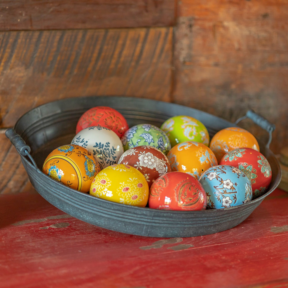 A close view of assorted brightly colored ceramic balls with floral and decorative patterns in a metal bowl.
