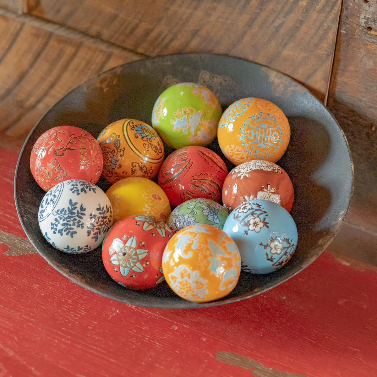 Close view of assorted bright ceramic balls with floral and ornamental patterns in a dark bowl.