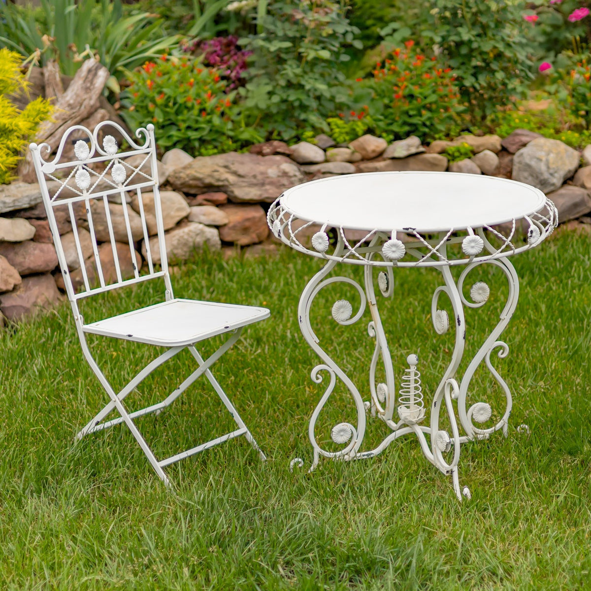 Antique white bistro table and one folding chair on grass, viewed at an angle