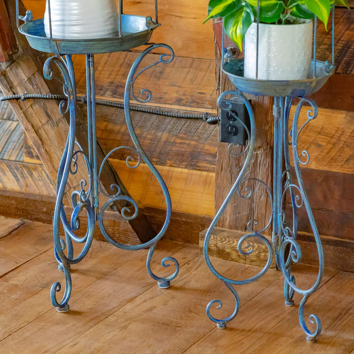 Two dark gray iron stands with round trays and ornate curling legs, shown with potted plants.