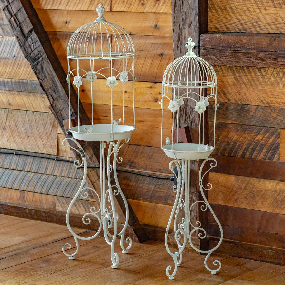 Two white iron birdcage planters with decorative flower details and curled legs, shown empty.