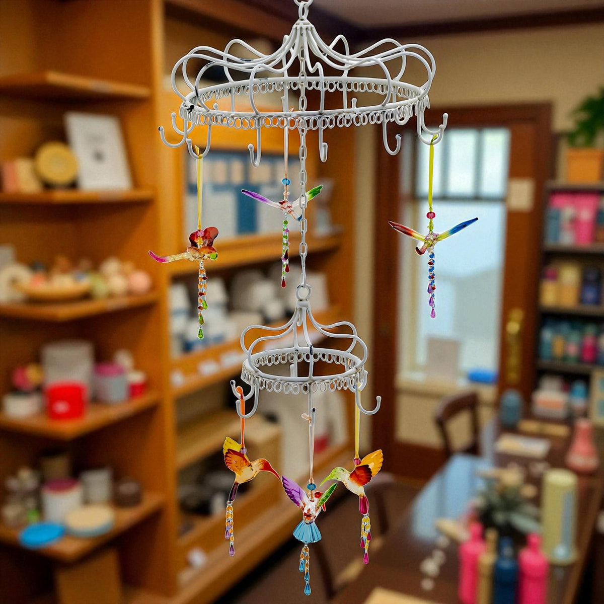 White metal hanging display holding small colorful birds and dangling decorations