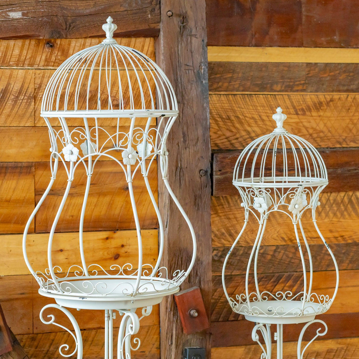 White hourglass birdcage plant stands shown together against a wood wall