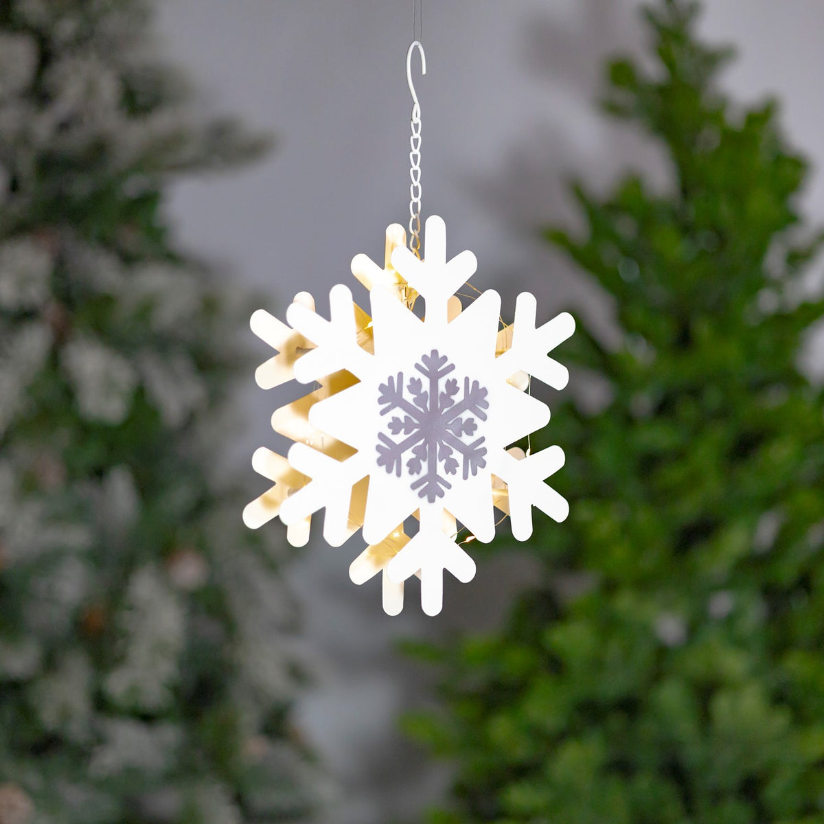 Close view of a white snowflake ornament with silver center and warm LED glow
