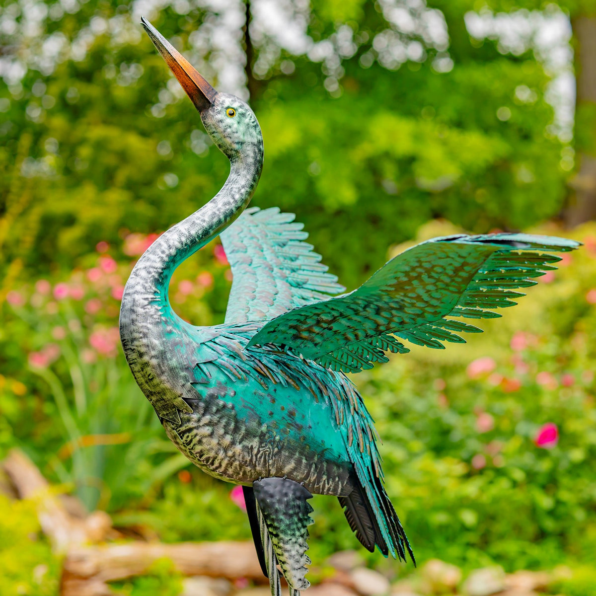 A teal heron sculpture with one wing spread, showing layered metal feathers and a long curved neck.