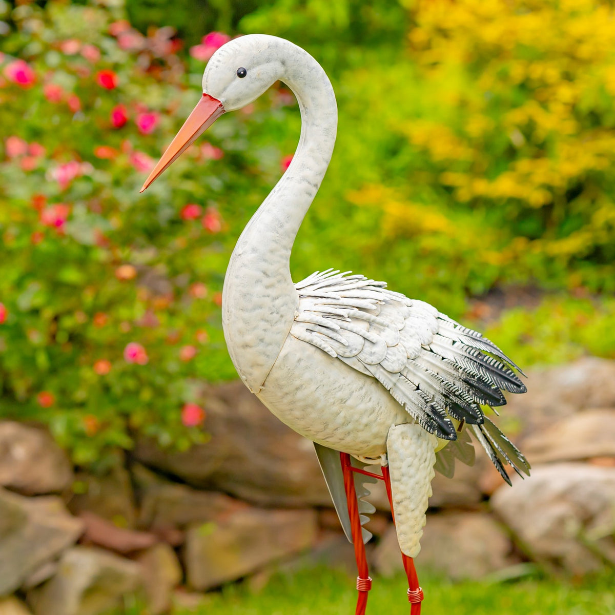 A white heron statue stands with its long orange beak and layered metal feathers visible.