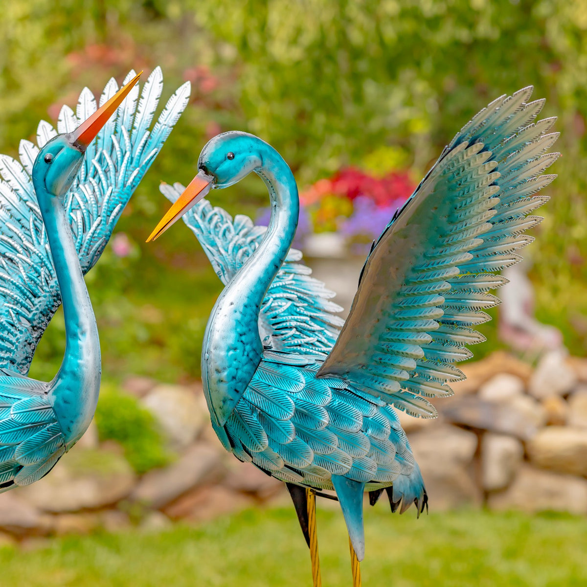 Close view of a blue-green crane figurine with raised wings in a garden