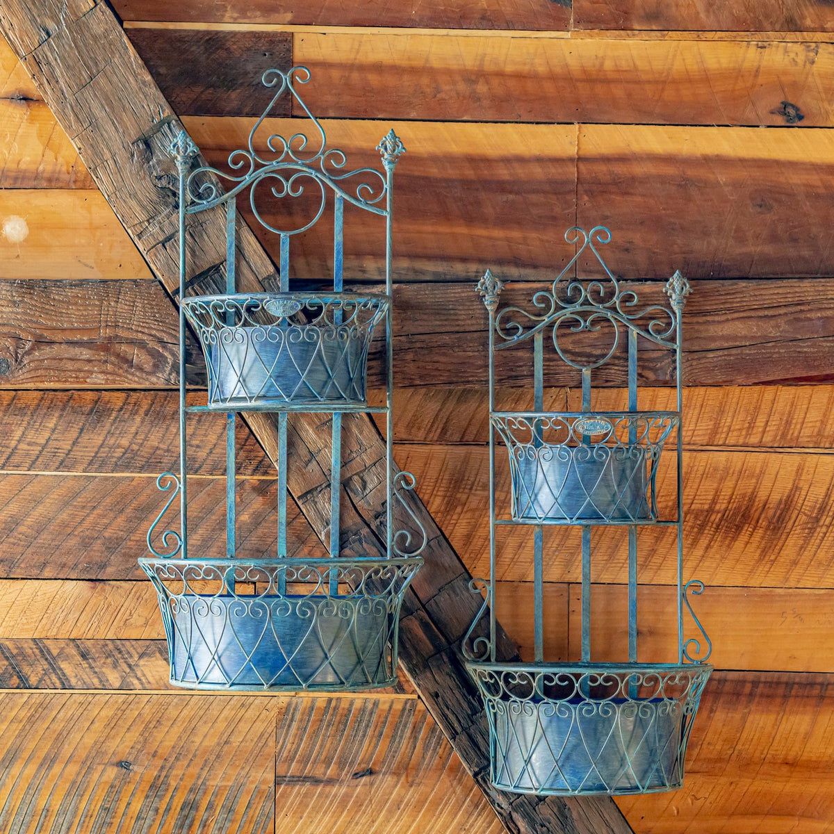 Pair of empty blue wall planters with decorative metalwork and removable baskets against a plank wall.
