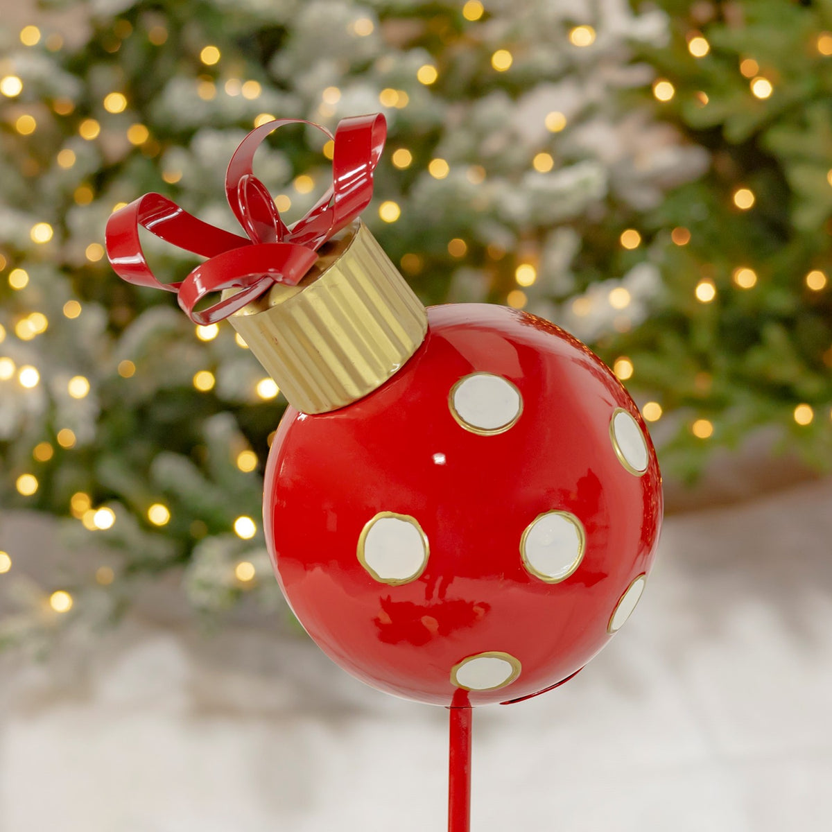 Close view of the glossy red ornament with white and gold dots, a gold cap, and red bow.