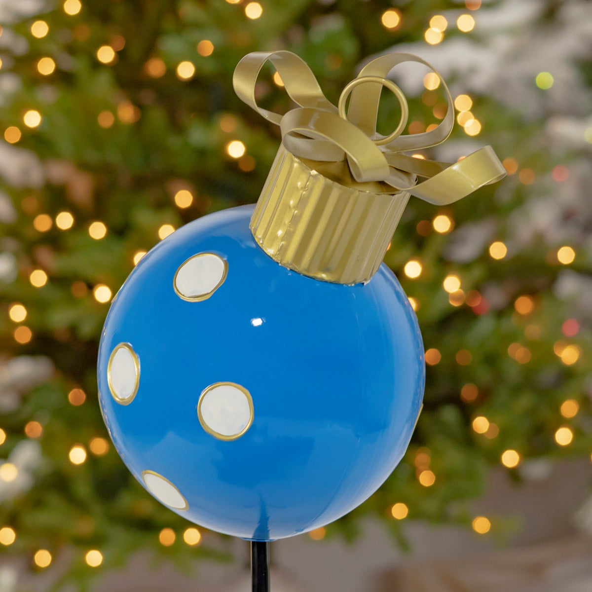 Glossy blue ornament with white and gold dots, topped by a ribbed gold cap and looping bow