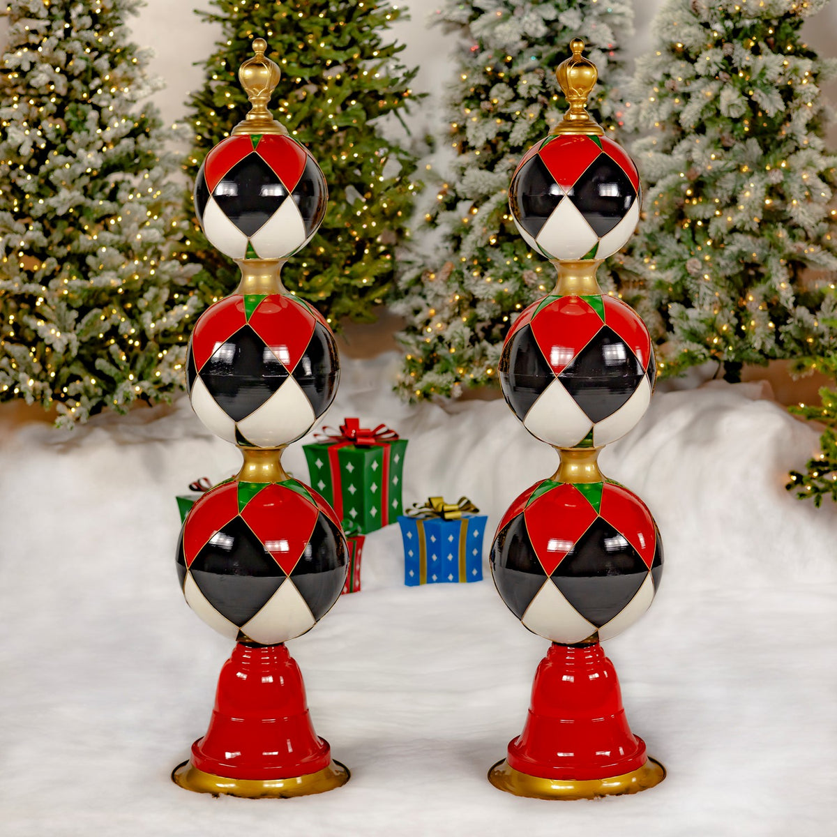 Two matching ornament towers stand side by side among wrapped gifts and snow-dusted trees.