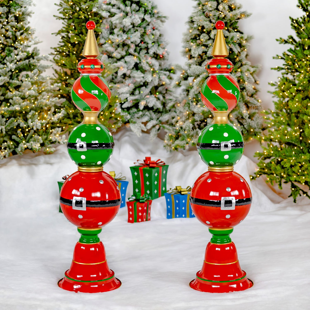 Two matching red and green ornament towers stand side by side in a snowy Christmas display.