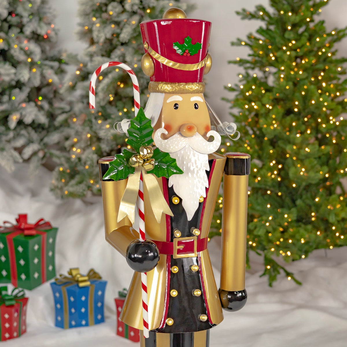 Closer front view of the nutcracker’s holly-trimmed hat, white beard, candy cane, and gold coat.