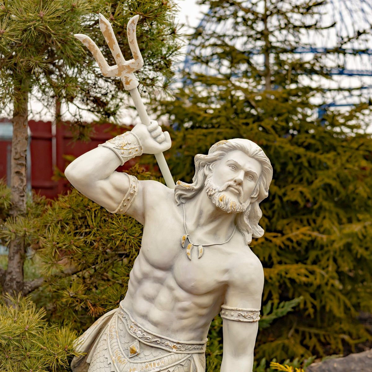 Close view of the merman’s bearded face, raised arm, and trident against evergreen branches.