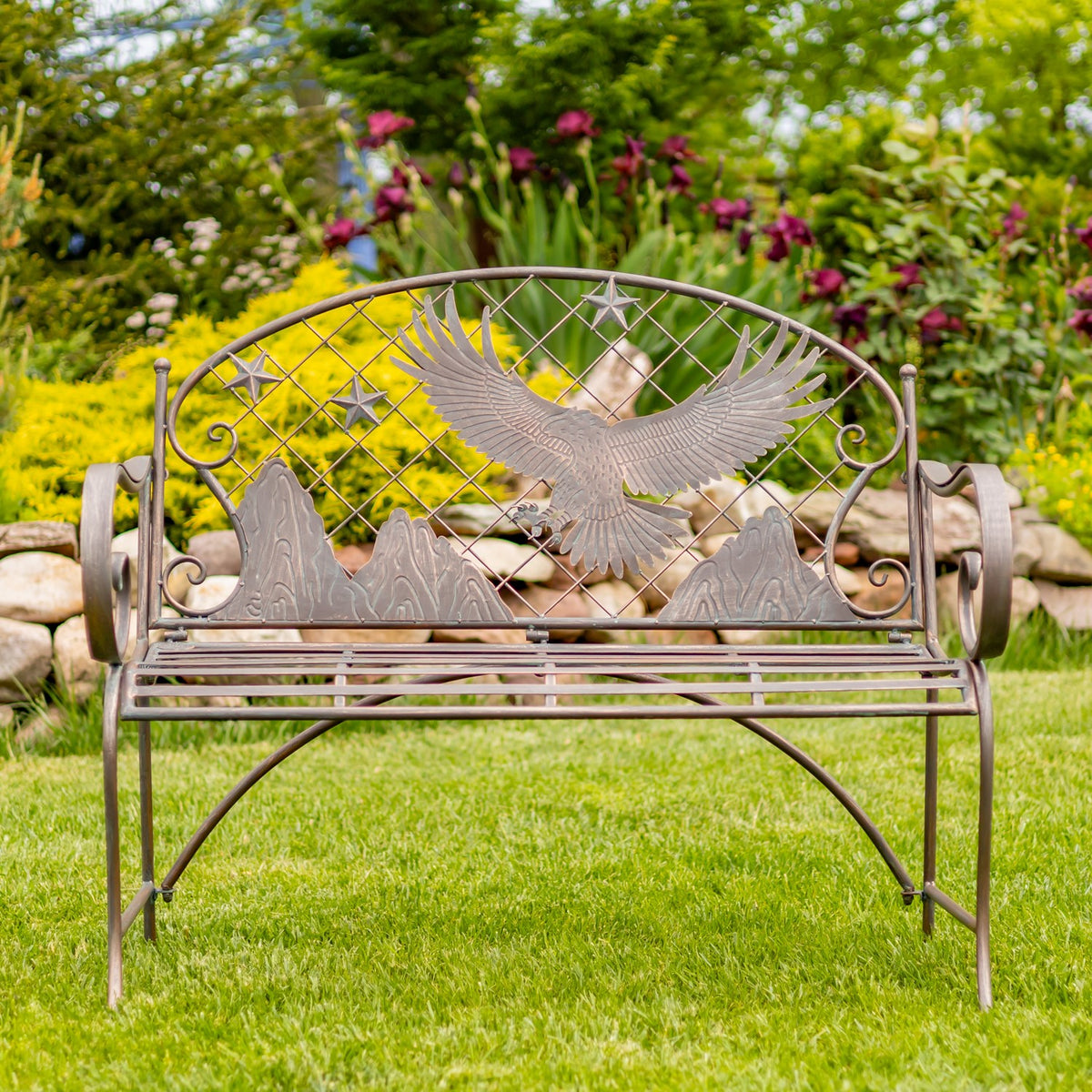 Front view of an iron garden bench with an eagle motif and curved arms among garden flowers.