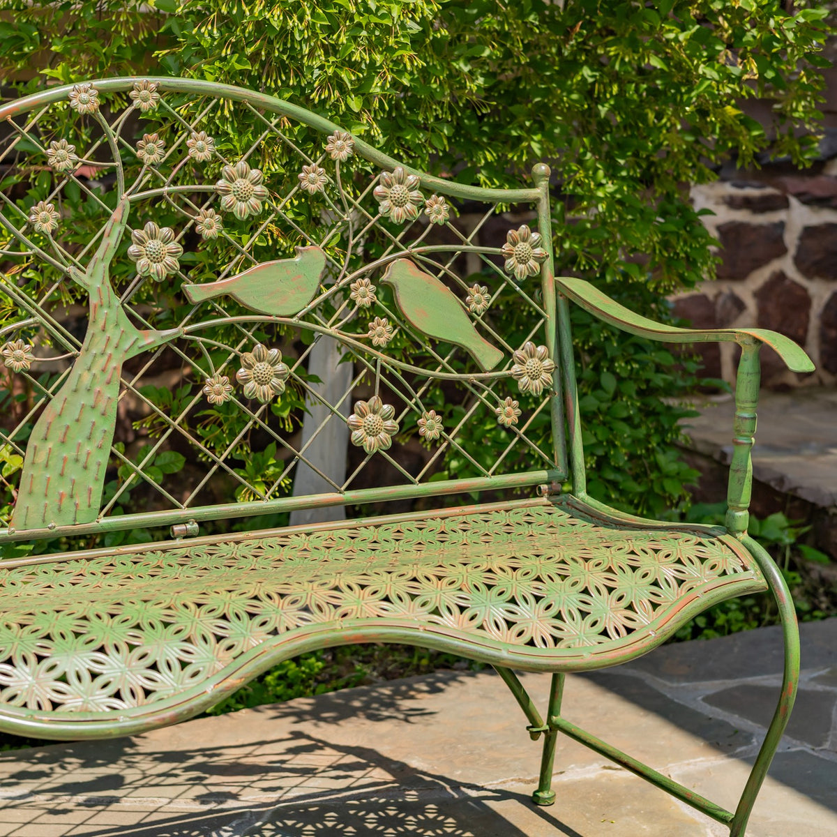 Close view of a green metal garden bench showing its floral backrest, bird motifs, and openwork seat.