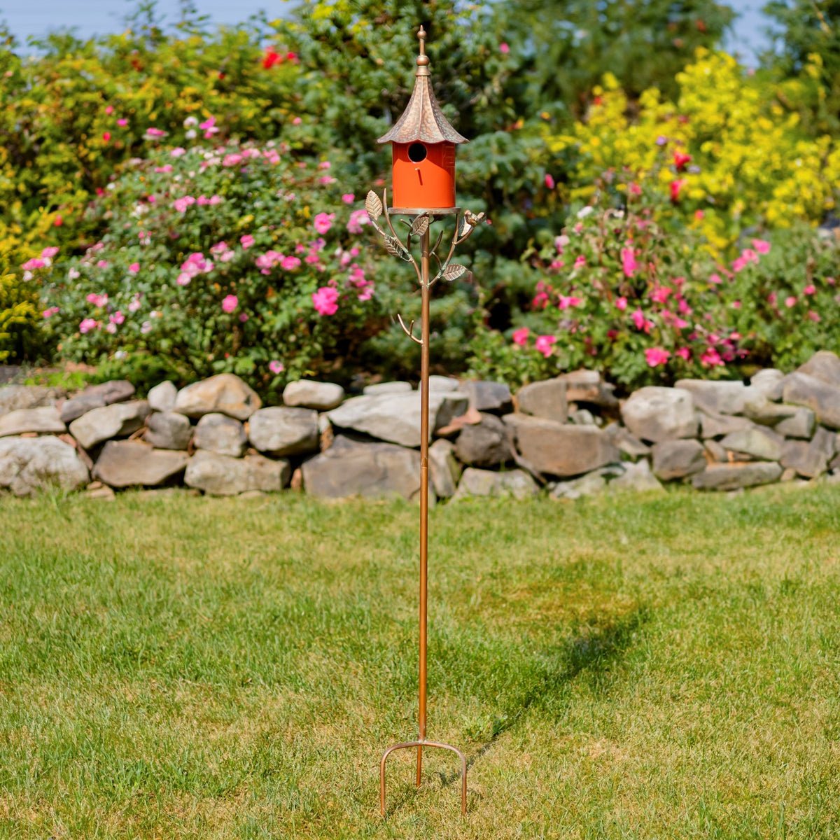 The full birdhouse stake stands in a lawn, with its slender pole and curved ground prongs visible.