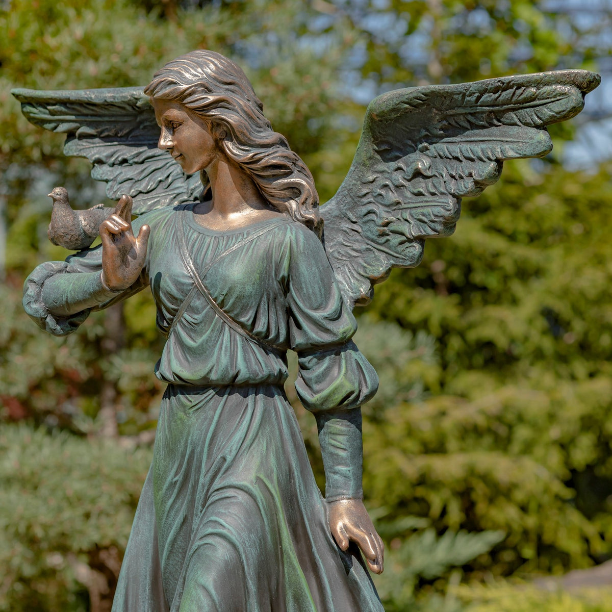 Closer view of the green-patina angel’s face, flowing hair, spread wings, and bird perched on her arm.