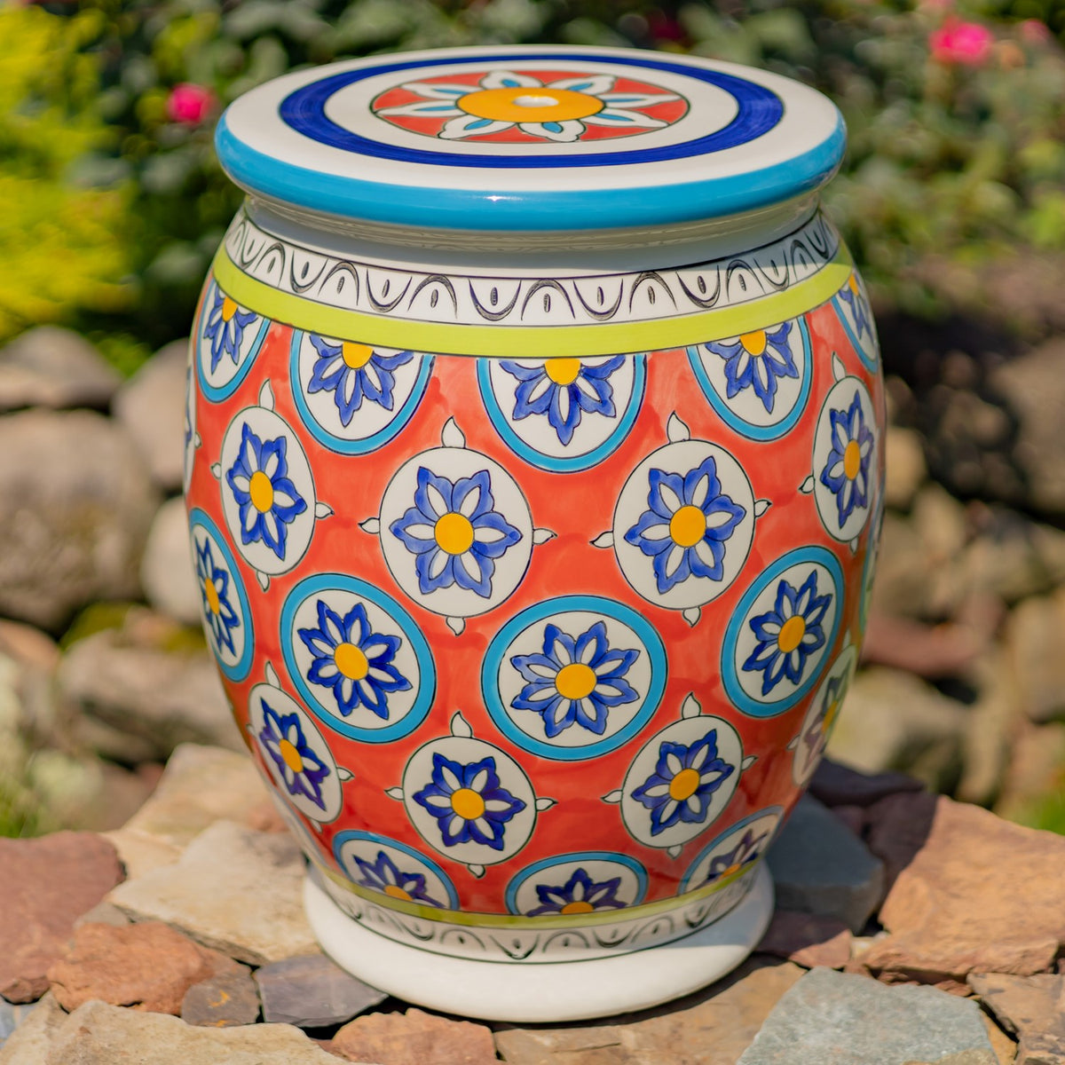 A close view of the rounded stool shows its coral body, blue floral motifs, and decorative top.
