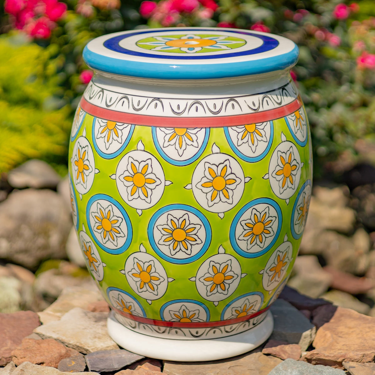 Close view of a green ceramic stool decorated with white and yellow flowers and colorful patterned bands.