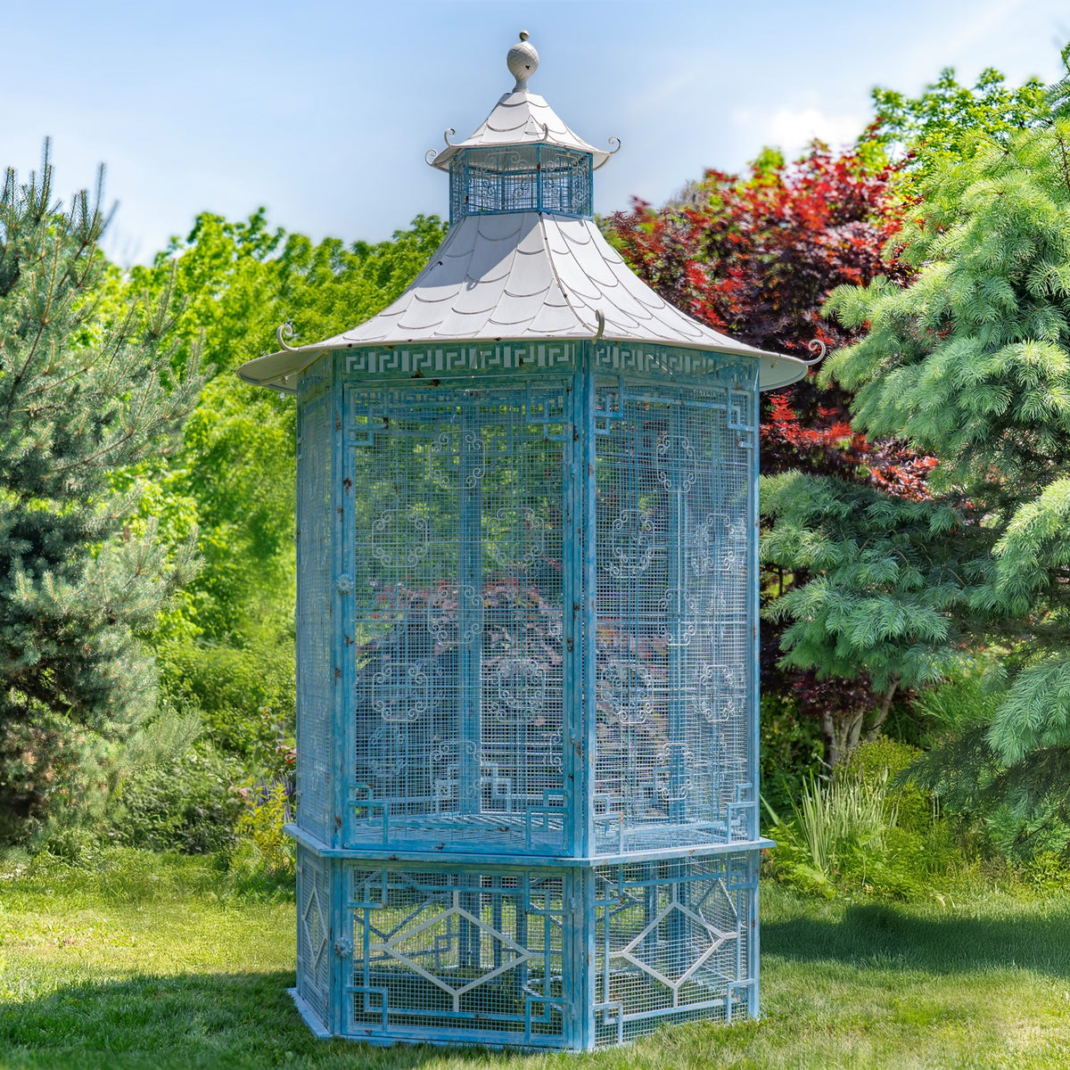 Blue-gray metal garden gazebo with lattice panels and a tiered pagoda-style roof among trees.