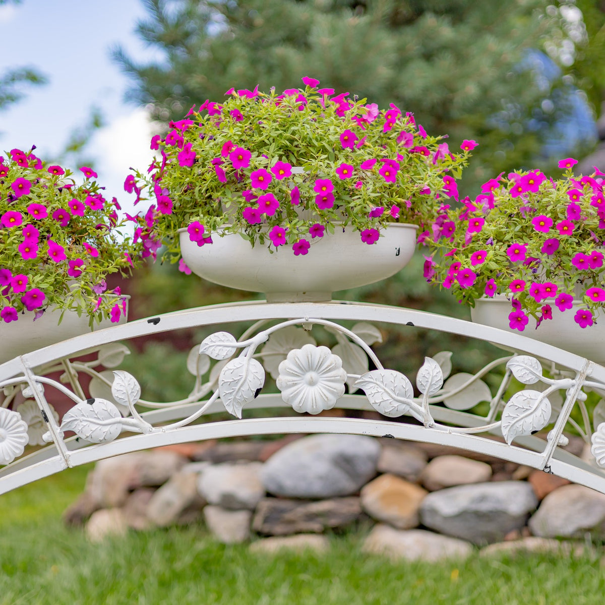 Close view of a flower-filled planter above the stand’s arched, leaf-and-flower metalwork.