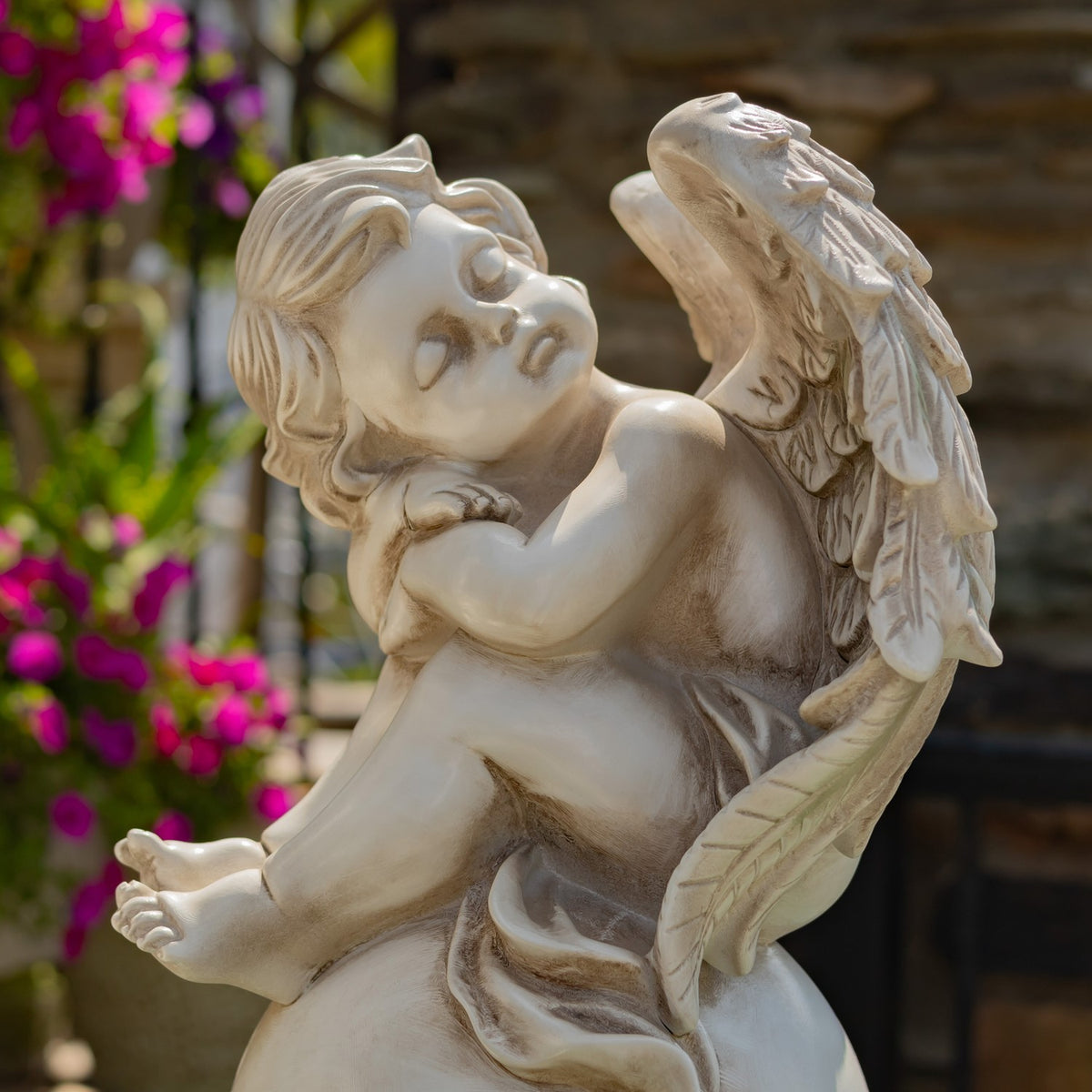 Close view of one pale cherub statue seated on a globe pedestal outdoors