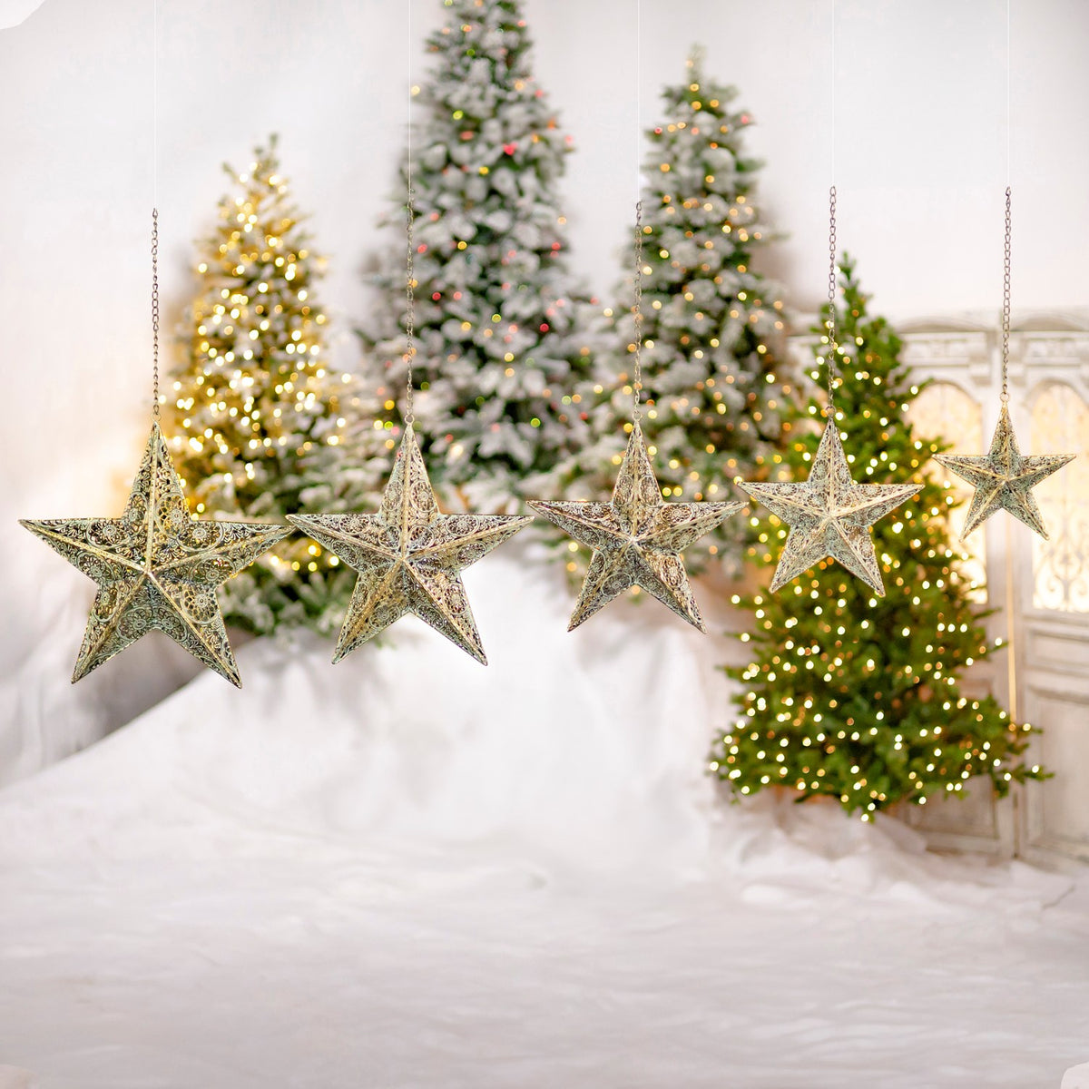 Several hanging gold star ornaments are displayed in a row against a festive backdrop of Christmas trees.