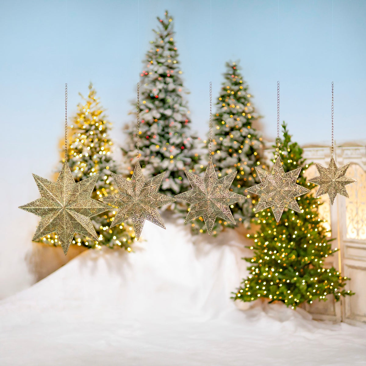Five openwork gold star ornaments hang at different heights against a festive tree display.