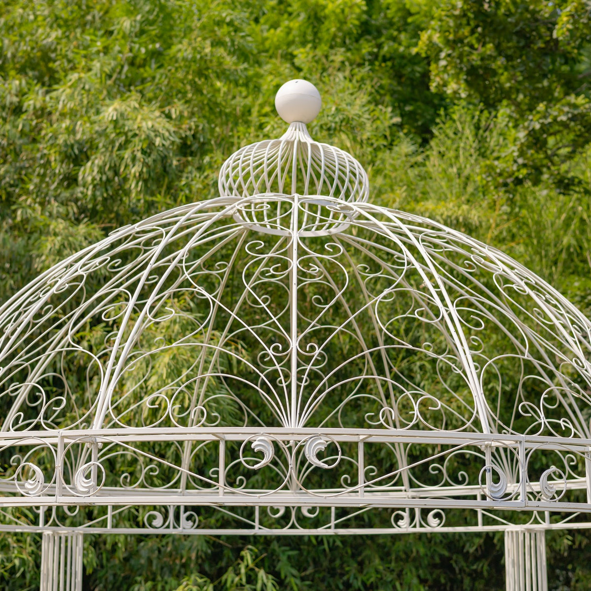 Close-up of the white gazebo’s domed iron roof, curled scrollwork, and round finial.
