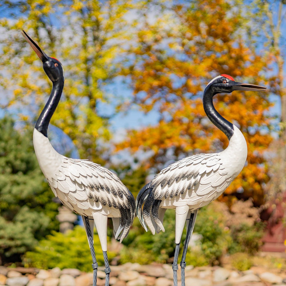 Two white crane figurines with dark necks shown close together outdoors