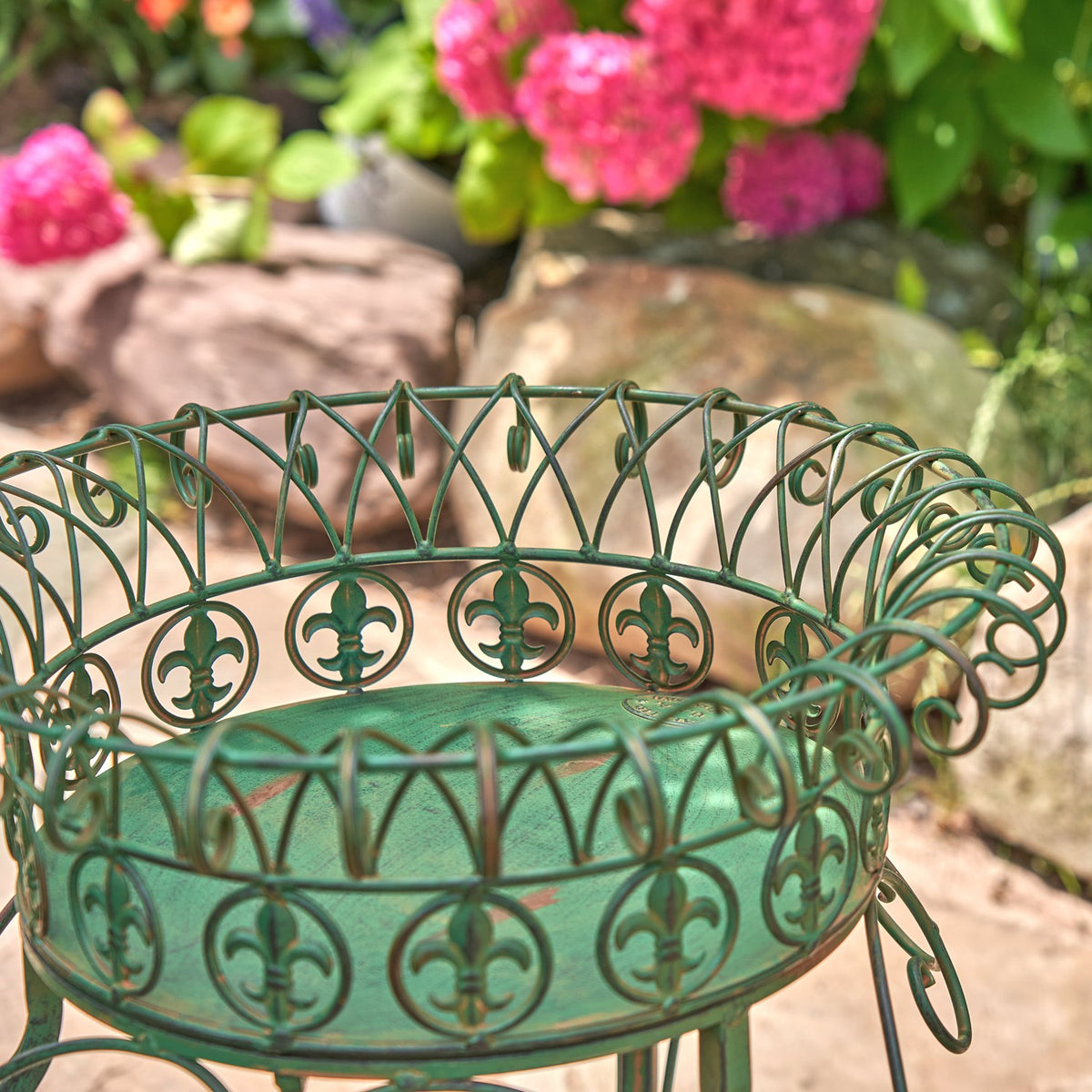 Close-up of an ornate green metal plant stand basket with curled wirework and circular floral motifs.