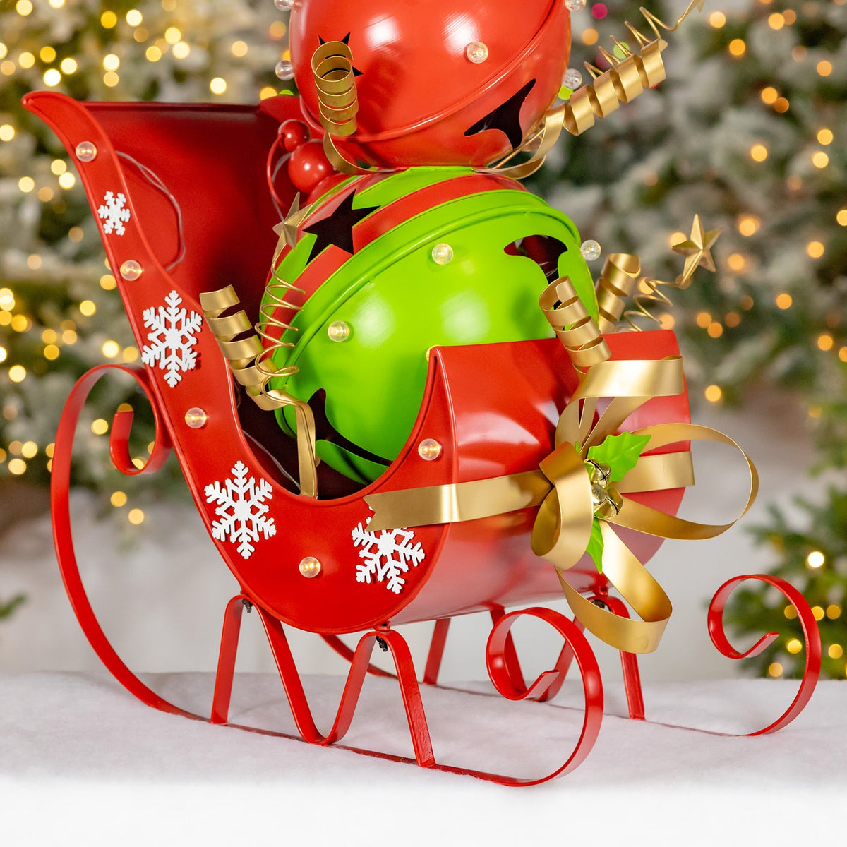 Close view of the red sleigh's curled runners, snowflake cutouts, gold ribbon and green figure.