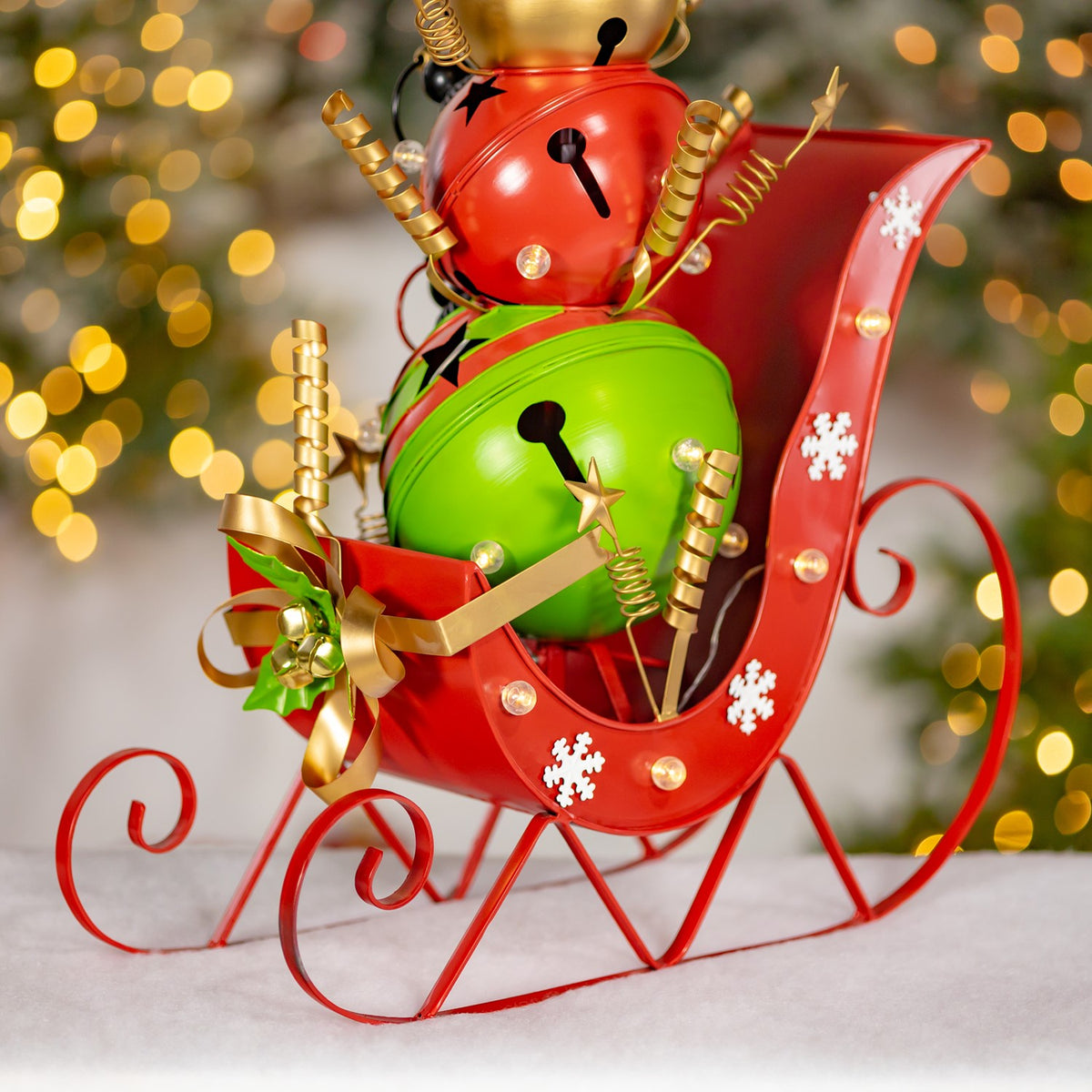 Closer view of the red sleigh’s curled runners, snowflake details and snowman with gold ribbon and bells.
