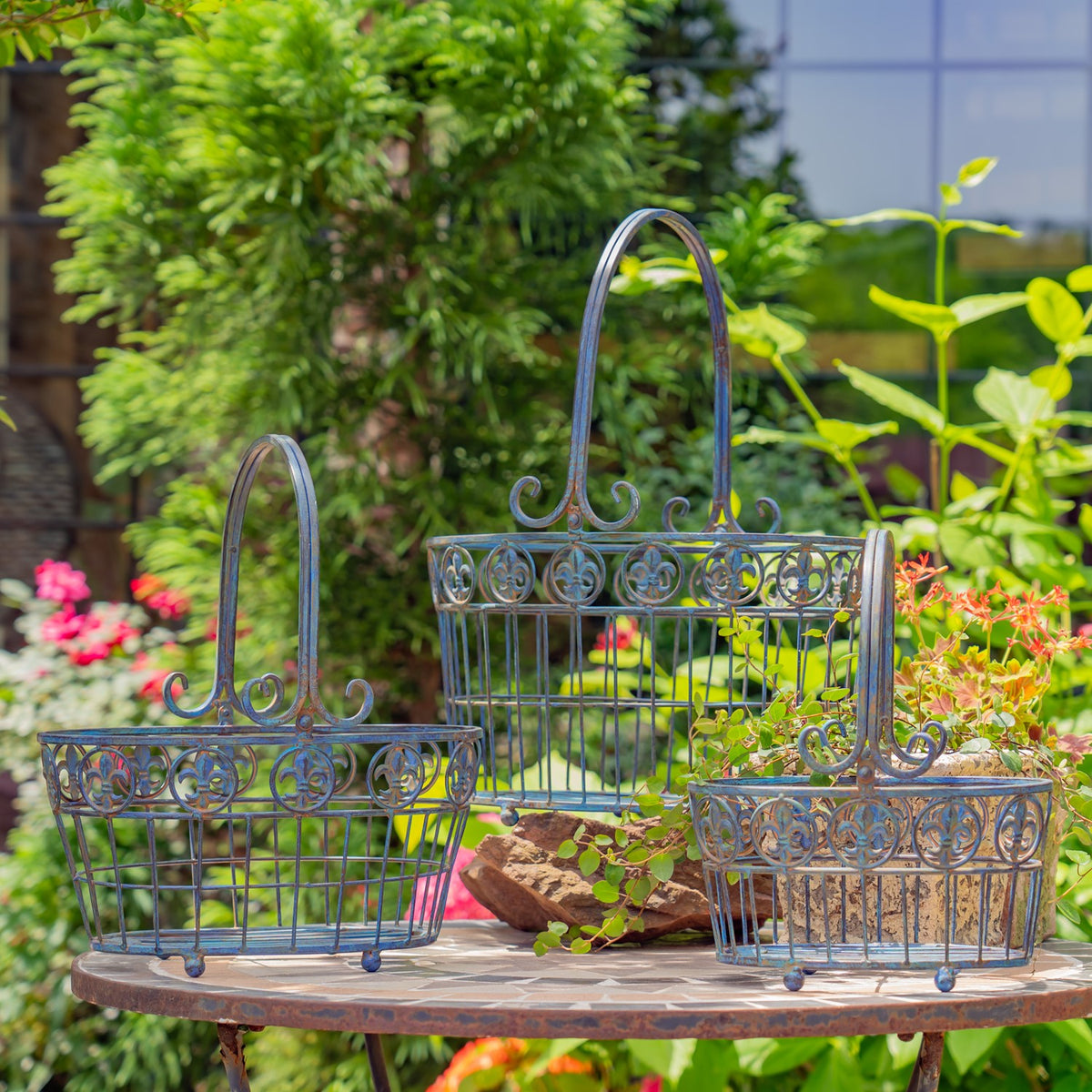 Three ornate iron wire baskets with tall handles arranged on a round garden table.