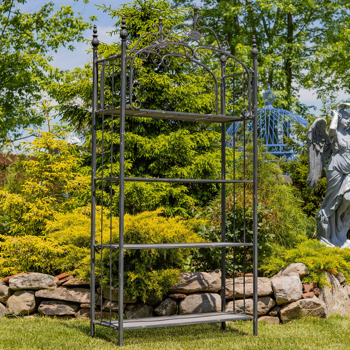 Tall black iron garden shelf with four mesh tiers and decorative scrollwork, shown empty.