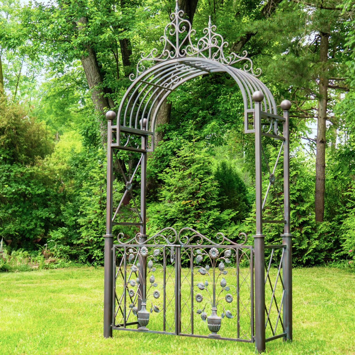 Full view of an ornate metal garden gate and tall arched trellis standing on a lawn.