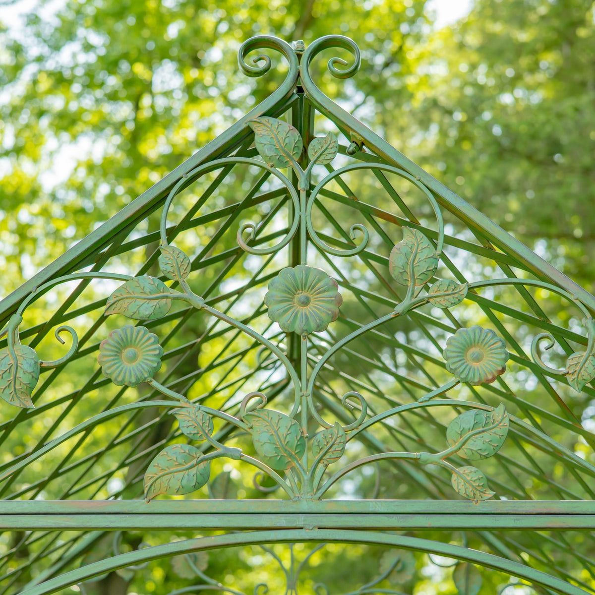 Front view of the arch's peaked ironwork, with symmetrical leaves, curling vines, and flower accents.