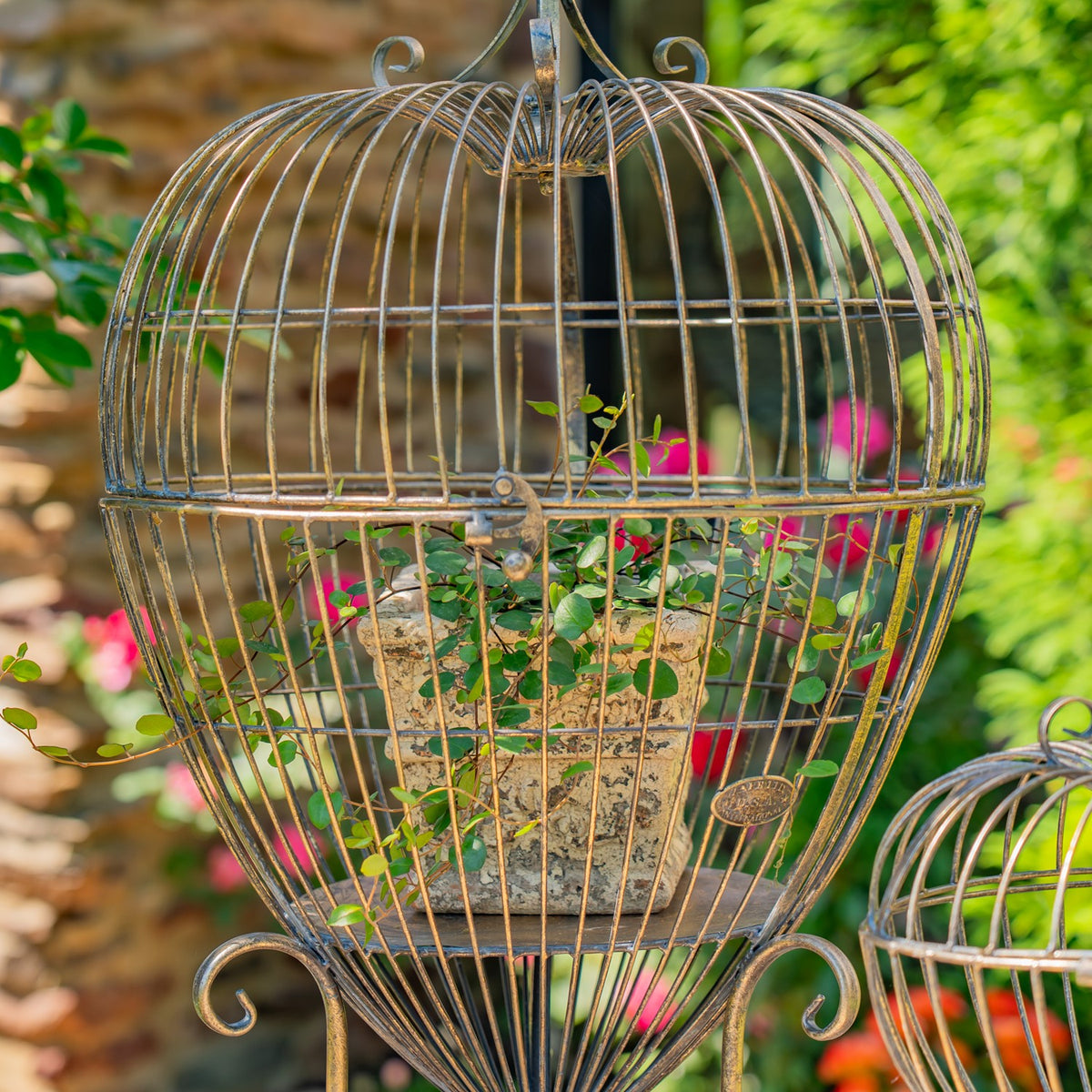 Large heart-shaped wire stand holding a potted plant, with part of a smaller matching stand at the edge.
