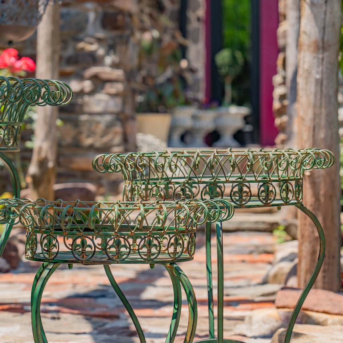 Green wire plant stands with curled legs and openwork baskets, arranged on a garden patio.